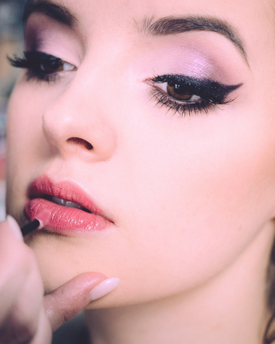woman with soft pink eyeshadow and smokey eyeliner has peach lipstick applied
